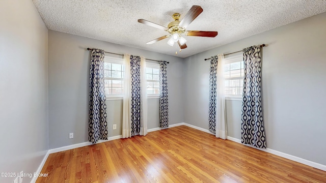 spare room featuring a wealth of natural light, a textured ceiling, baseboards, and wood finished floors