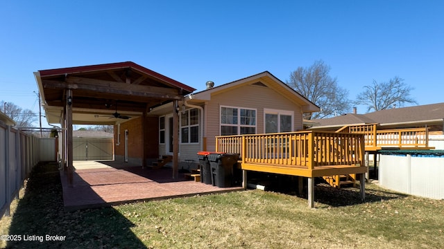 back of house with a lawn, a fenced backyard, a covered pool, a wooden deck, and a patio area