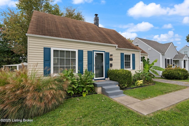 cape cod-style house featuring a shingled roof, a chimney, and a front lawn