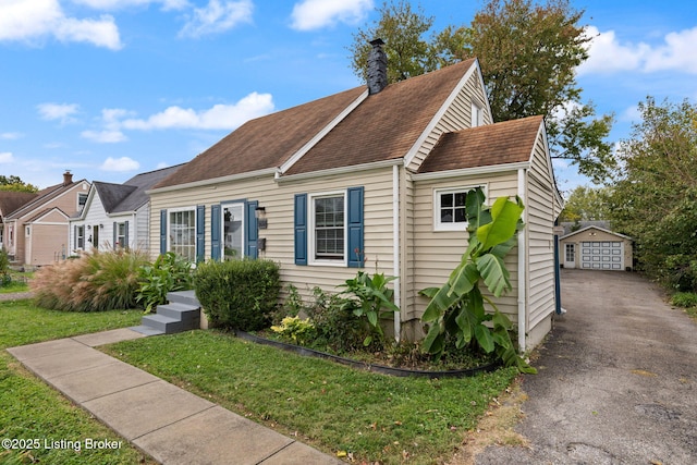 view of front of home with a front lawn, a chimney, an outdoor structure, and a detached garage