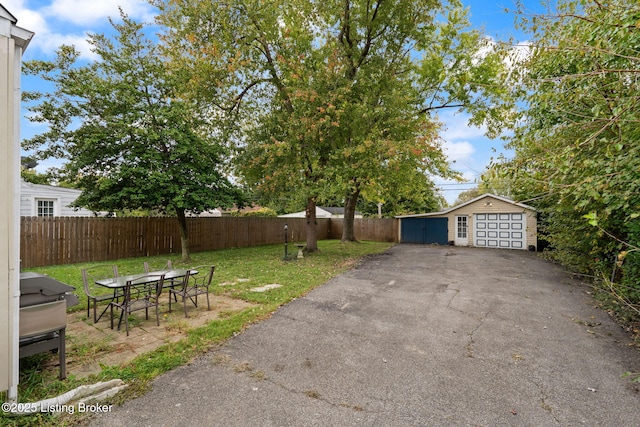 view of yard featuring an outbuilding, aphalt driveway, outdoor dining area, fence private yard, and a detached garage