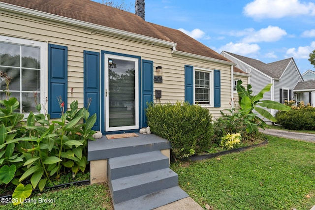 entrance to property featuring a shingled roof and a yard