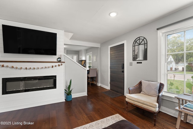 living area featuring dark wood-type flooring, a glass covered fireplace, a wealth of natural light, and baseboards