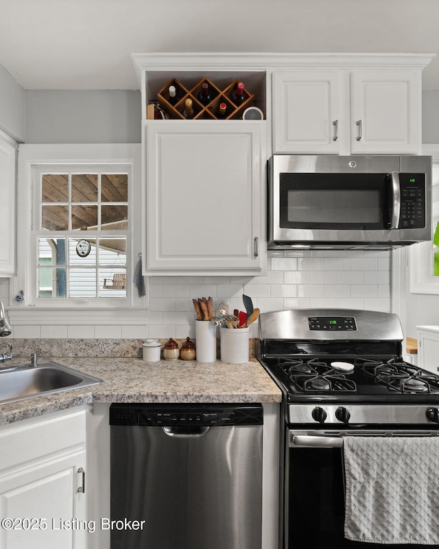 kitchen with tasteful backsplash, light countertops, appliances with stainless steel finishes, white cabinetry, and a sink