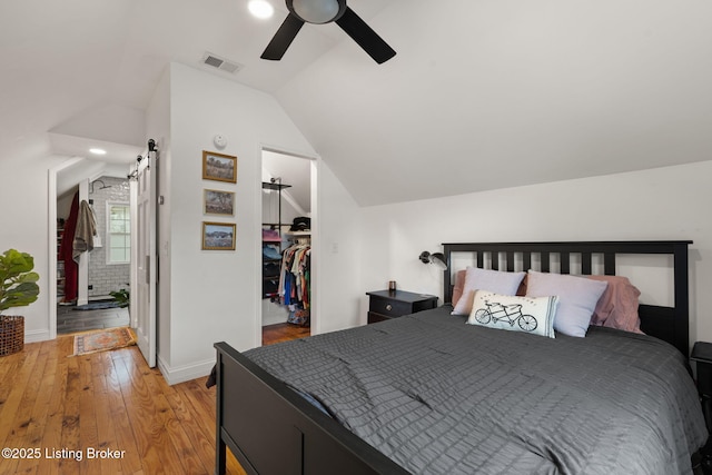 bedroom with a walk in closet, lofted ceiling, wood-type flooring, visible vents, and a ceiling fan