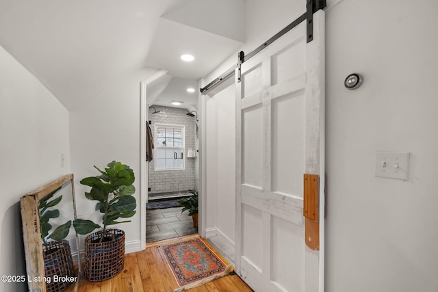 hall with lofted ceiling, a barn door, and wood finished floors