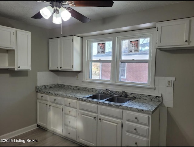 kitchen featuring white cabinetry, a sink, a textured ceiling, wood finished floors, and baseboards