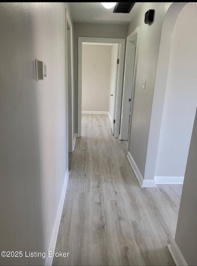 hallway with light wood finished floors, visible vents, and baseboards