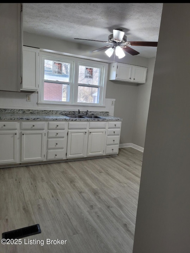 kitchen featuring light wood-style floors, a textured ceiling, white cabinetry, and a sink