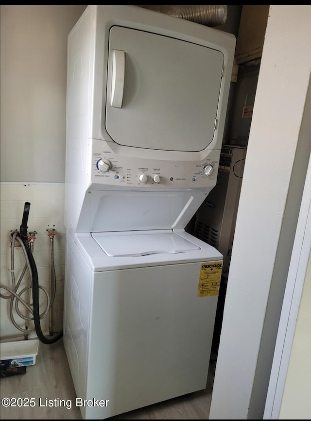 washroom with tile walls, light wood-style floors, wainscoting, stacked washing maching and dryer, and laundry area