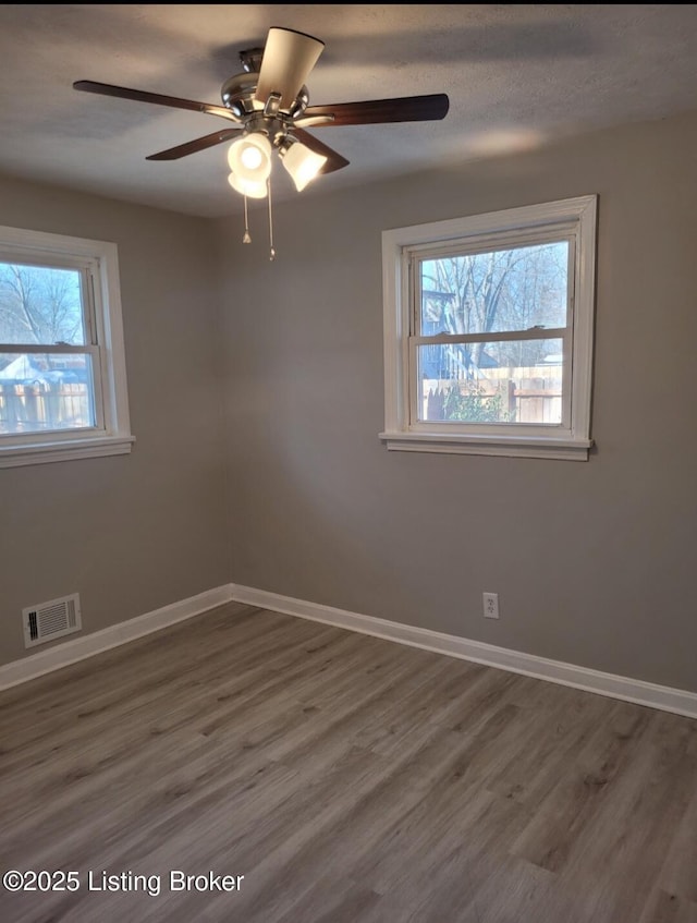 empty room with dark wood-type flooring, visible vents, and baseboards