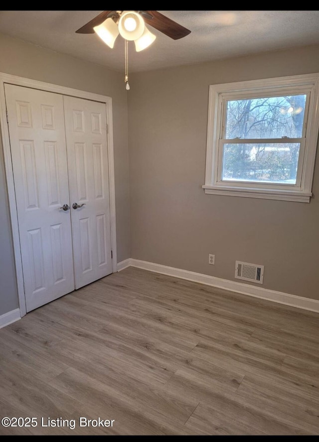 unfurnished bedroom featuring baseboards, visible vents, a ceiling fan, light wood-style floors, and a closet