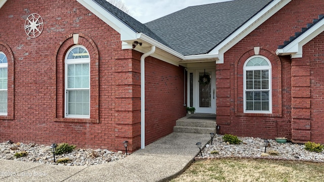 property entrance with a shingled roof and brick siding