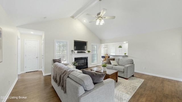 living area with beam ceiling, high vaulted ceiling, wood finished floors, and a glass covered fireplace