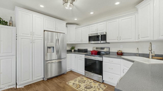 kitchen featuring stainless steel appliances, white cabinets, a sink, and wood finished floors