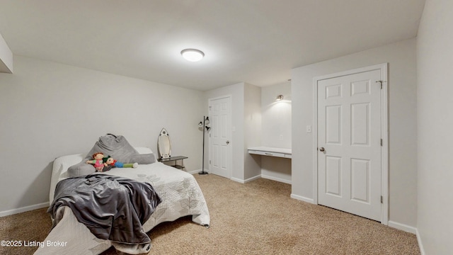 bedroom featuring baseboards, built in study area, and light colored carpet