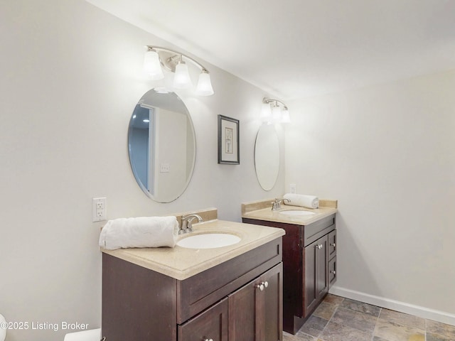 bathroom with stone finish flooring, baseboards, two vanities, and a sink