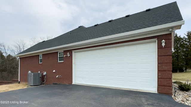 view of side of property with central AC, brick siding, driveway, and roof with shingles