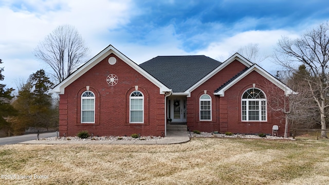 ranch-style home featuring a shingled roof, a front yard, fence, and brick siding