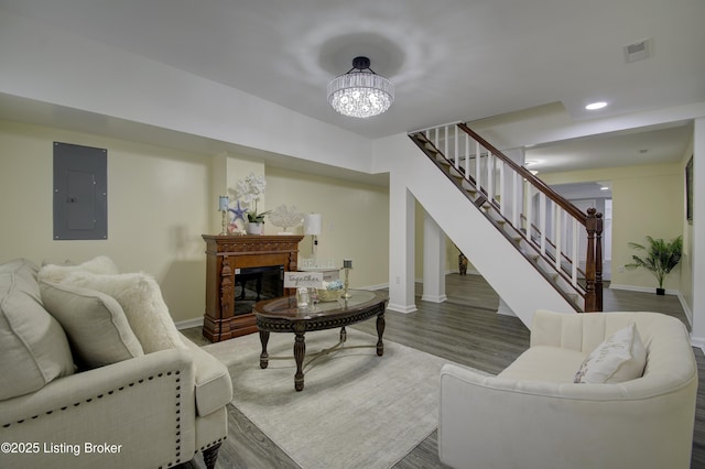 living room featuring dark wood-style floors, visible vents, stairway, a glass covered fireplace, and electric panel