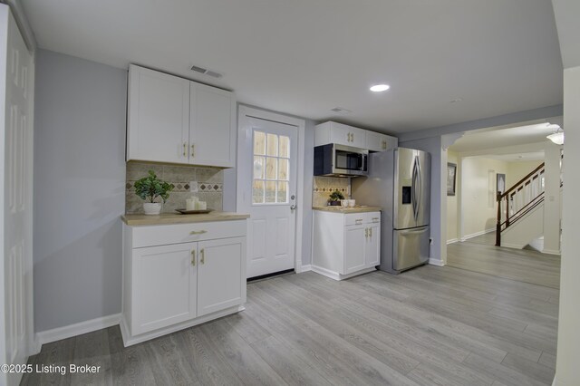 kitchen featuring stainless steel appliances, white cabinetry, light wood-style floors, light countertops, and decorative backsplash