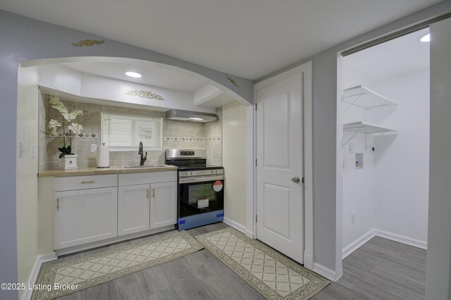 kitchen with stainless steel stove, a sink, white cabinetry, light wood-style floors, and wall chimney range hood