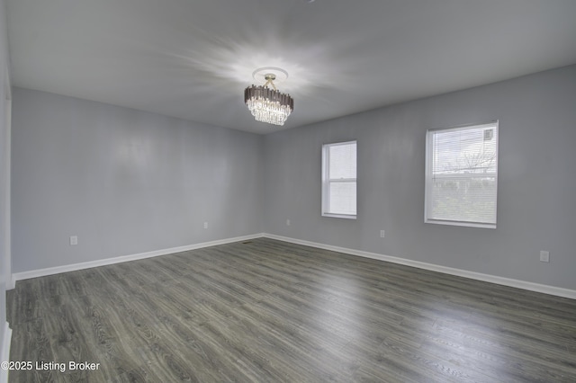 spare room featuring a chandelier, dark wood-type flooring, and baseboards