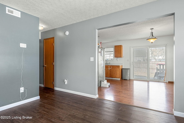 spare room with dark wood-type flooring, visible vents, and baseboards