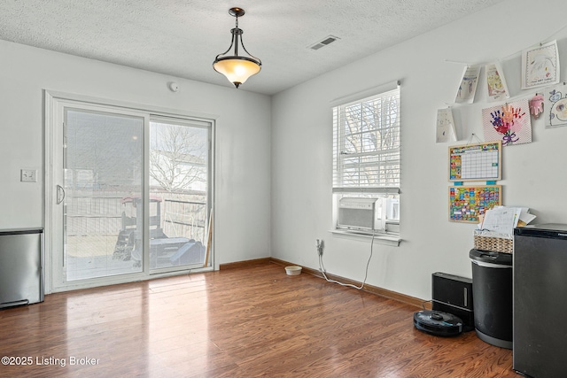 empty room featuring baseboards, visible vents, wood finished floors, cooling unit, and a textured ceiling