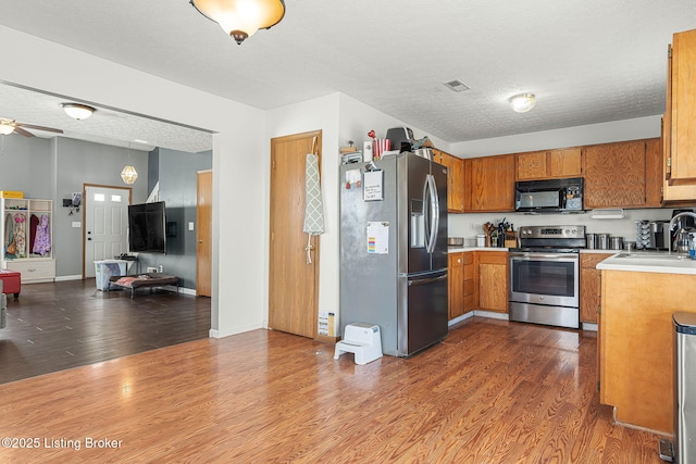 kitchen with appliances with stainless steel finishes, brown cabinets, dark wood-type flooring, light countertops, and a sink