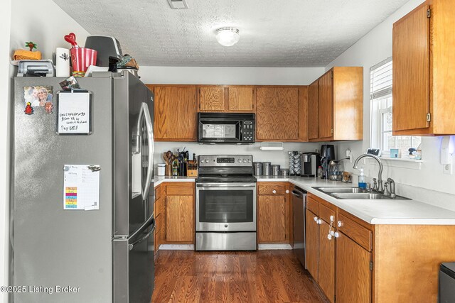 kitchen with dark wood-type flooring, appliances with stainless steel finishes, brown cabinets, and a sink