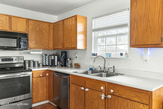 kitchen featuring a textured ceiling, a sink, light countertops, appliances with stainless steel finishes, and brown cabinets