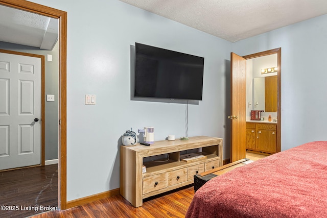 bedroom with a textured ceiling, wood finished floors, connected bathroom, and baseboards