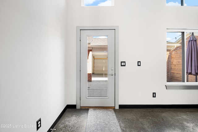 doorway with finished concrete floors, a towering ceiling, and baseboards