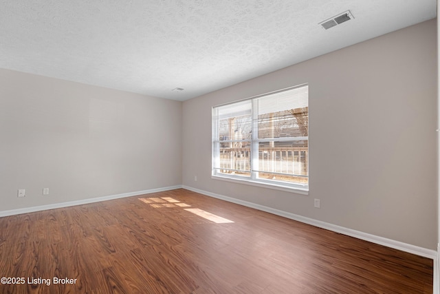 spare room featuring a textured ceiling, wood finished floors, visible vents, and baseboards