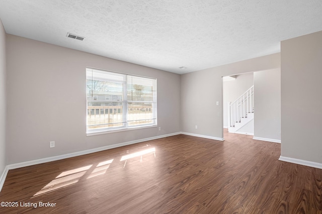 unfurnished room featuring a textured ceiling, dark wood-type flooring, visible vents, baseboards, and stairs