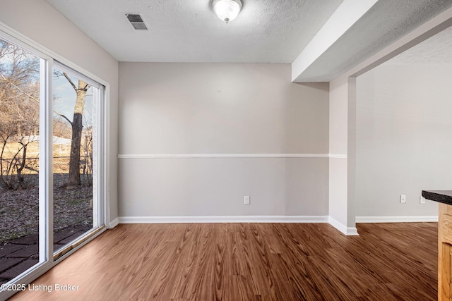 unfurnished room featuring visible vents, a textured ceiling, baseboards, and wood finished floors