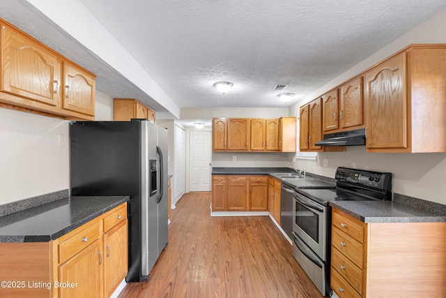 kitchen with stainless steel appliances, dark countertops, a textured ceiling, light wood-type flooring, and under cabinet range hood