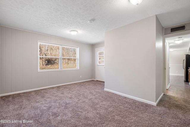 spare room featuring a textured ceiling, carpet, visible vents, and baseboards