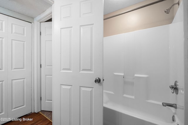 bathroom with shower / tub combination, a textured ceiling, and wood finished floors