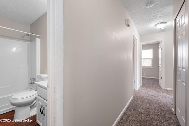 corridor with carpet flooring, a textured ceiling, and baseboards