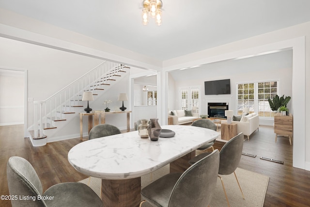 dining room with dark wood-style flooring, stairway, a glass covered fireplace, and baseboards