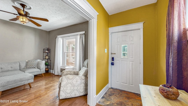 foyer with ceiling fan, a textured ceiling, baseboards, and wood finished floors