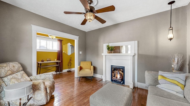 living room featuring a fireplace with flush hearth, a ceiling fan, baseboards, and hardwood / wood-style flooring