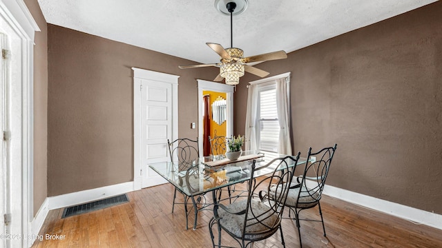 dining room featuring visible vents, a textured wall, hardwood / wood-style floors, ceiling fan, and baseboards