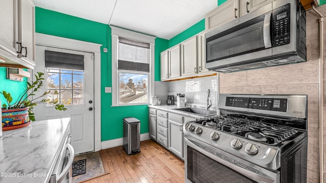 kitchen with backsplash, appliances with stainless steel finishes, a sink, light wood-type flooring, and baseboards