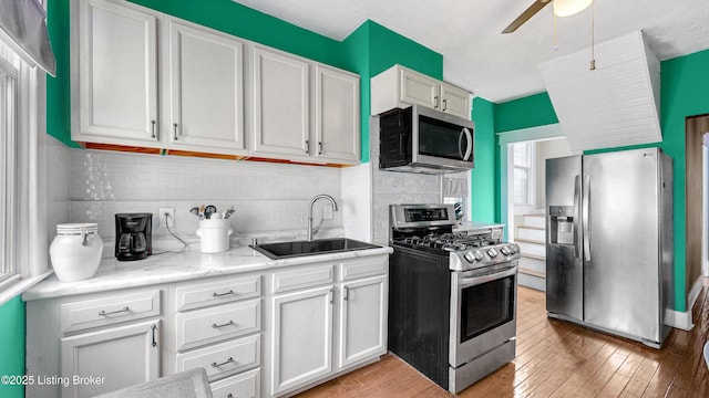 kitchen featuring light wood finished floors, decorative backsplash, appliances with stainless steel finishes, white cabinetry, and a sink