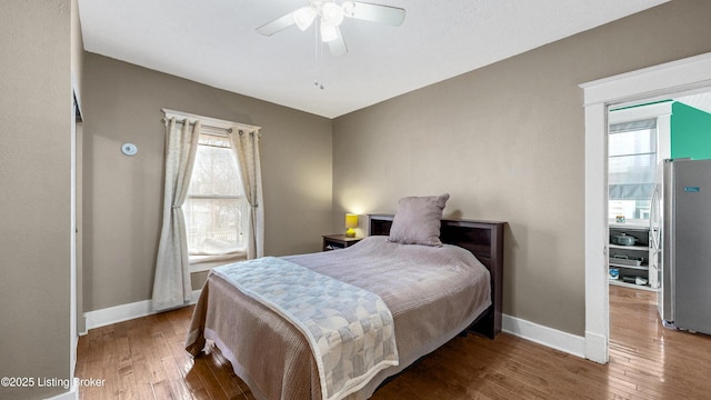 bedroom featuring multiple windows, wood-type flooring, freestanding refrigerator, and baseboards