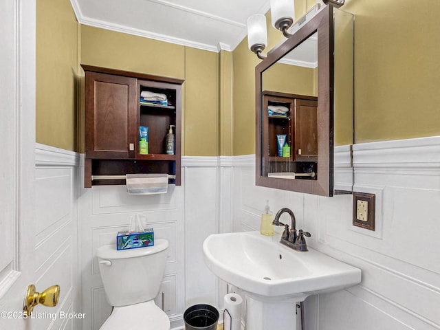 bathroom featuring toilet, a decorative wall, a wainscoted wall, a sink, and ornamental molding