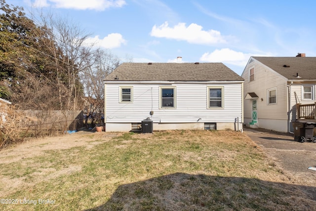 rear view of house with a shingled roof, central AC, fence, and a lawn